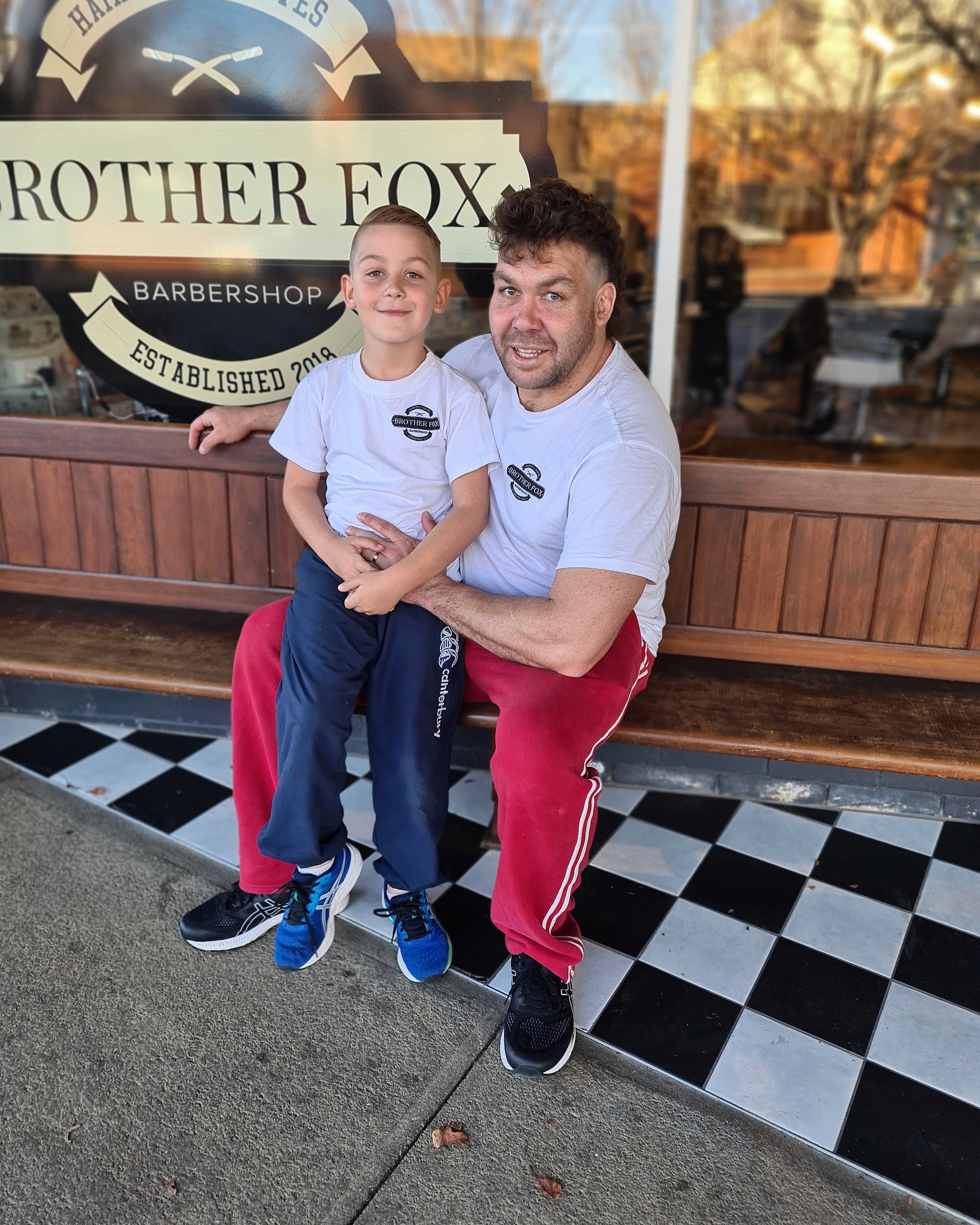 A man and a young boy in Brother Fox t-shirts on the bench outside the shop, under the Established 2018 window sign
