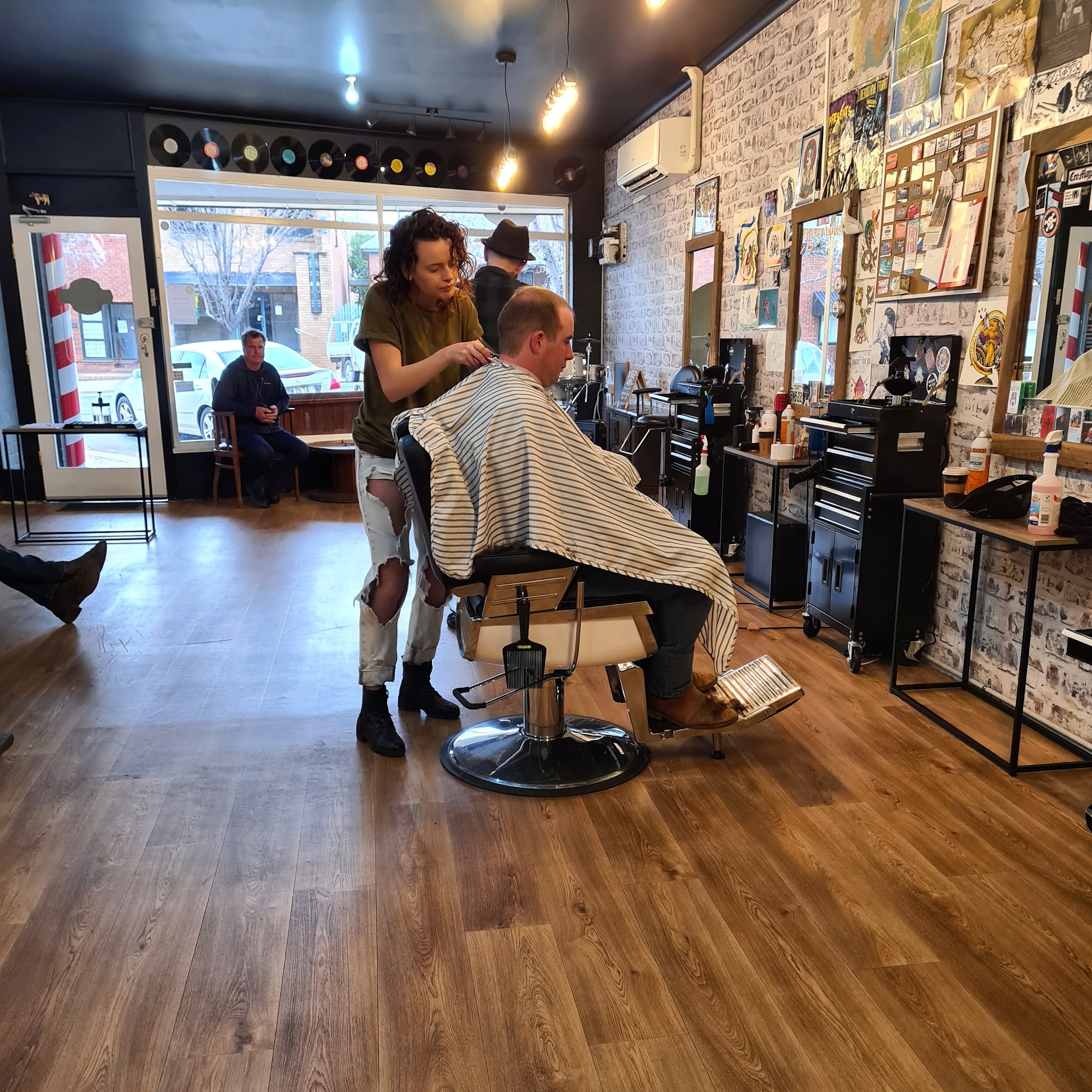 A barber cutting a client's hair on the shop floor at Brother Fox, Kendal Street visible through the window