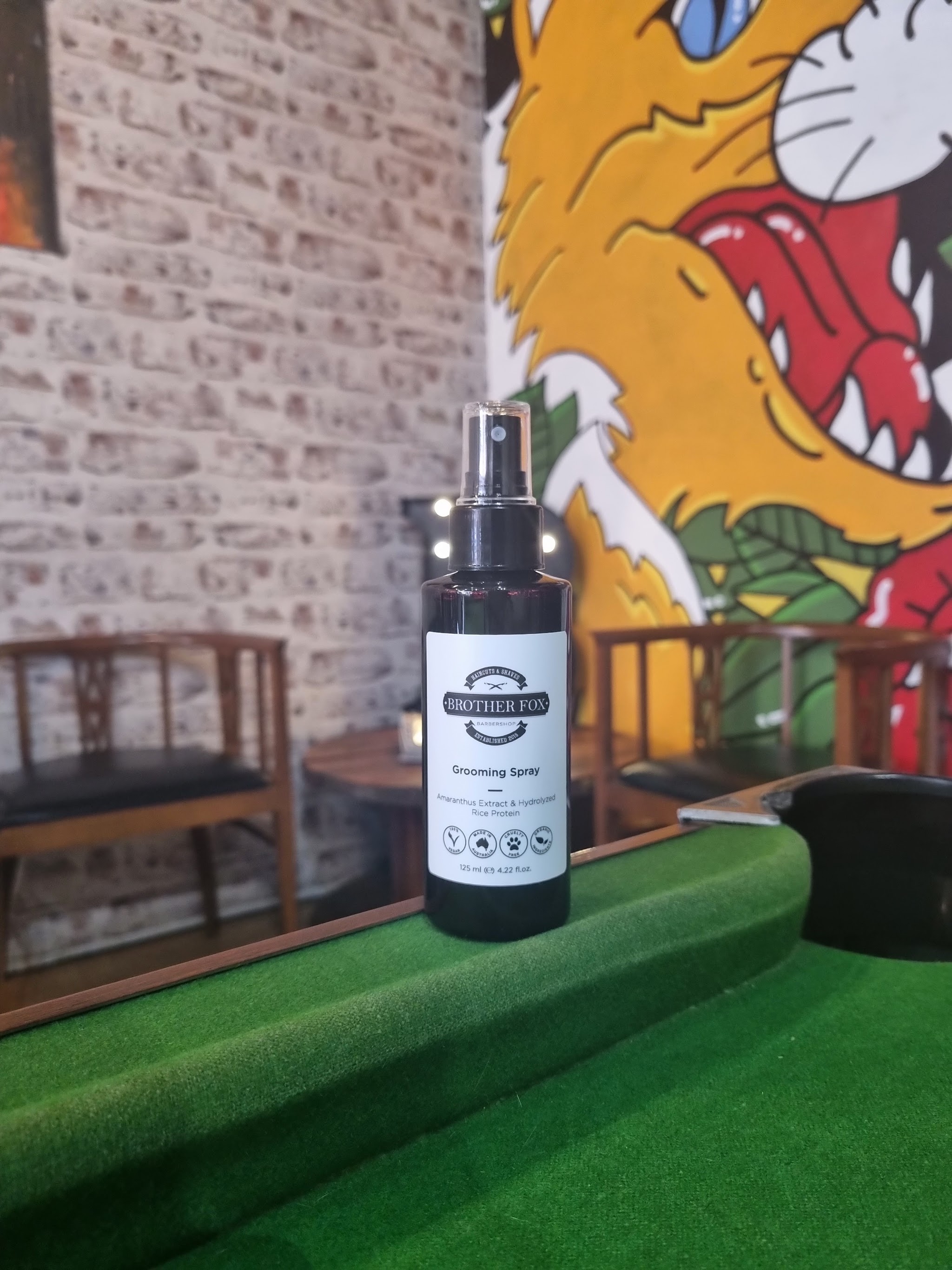 Brother Fox Barbershop grooming spray on the pool table in front of the shop's fox mural