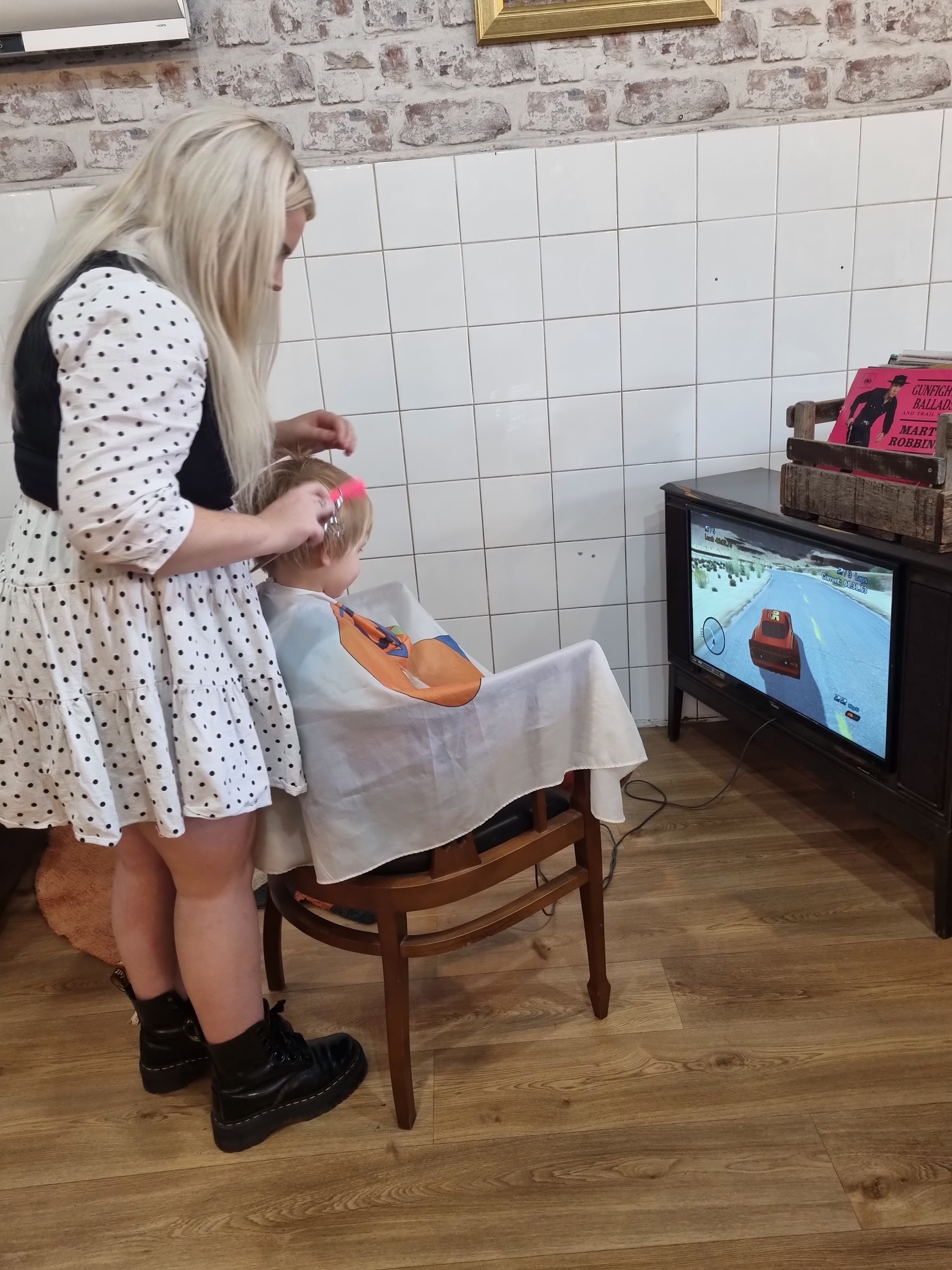 A Brother Fox barber cutting a young boy's hair while he plays a racing game on an old TV